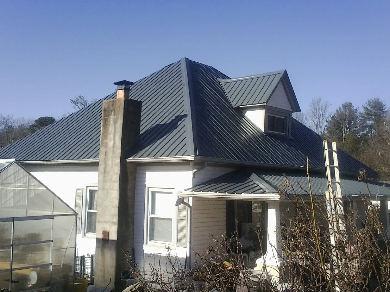 Dark blue standing seam metal roof on a white farmhouse with dormer — Slate & Tile Roof Repair by Roofing Brothers in South Bloomingville