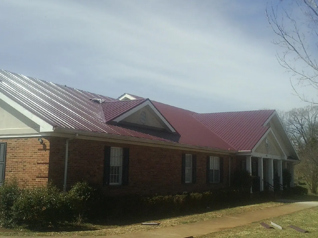 Red metal roof with gabled entries on a long brick building, from a Hail Damage Roof Repair job in South Bloomingville