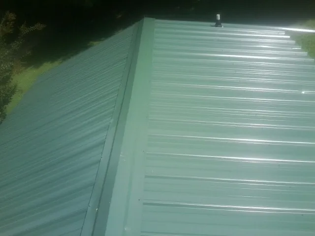 New green metal panels meeting at the ridge of a roof — Flat Roof Repair work by our crew in South Bloomingville