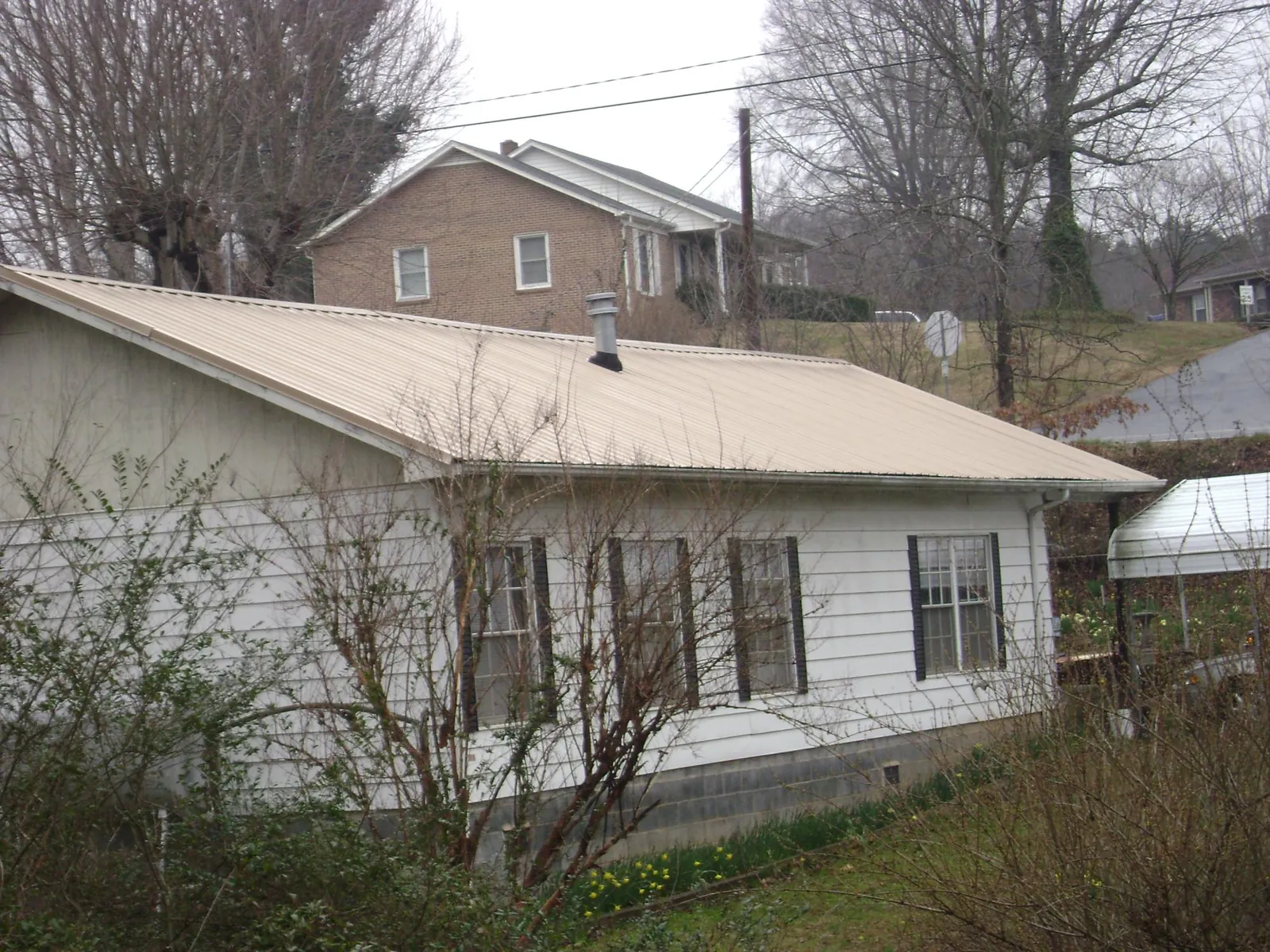 Tan metal roof on a white sided house set into a hillside — Commercial Roofing by Roofing Brothers in South Bloomingville
